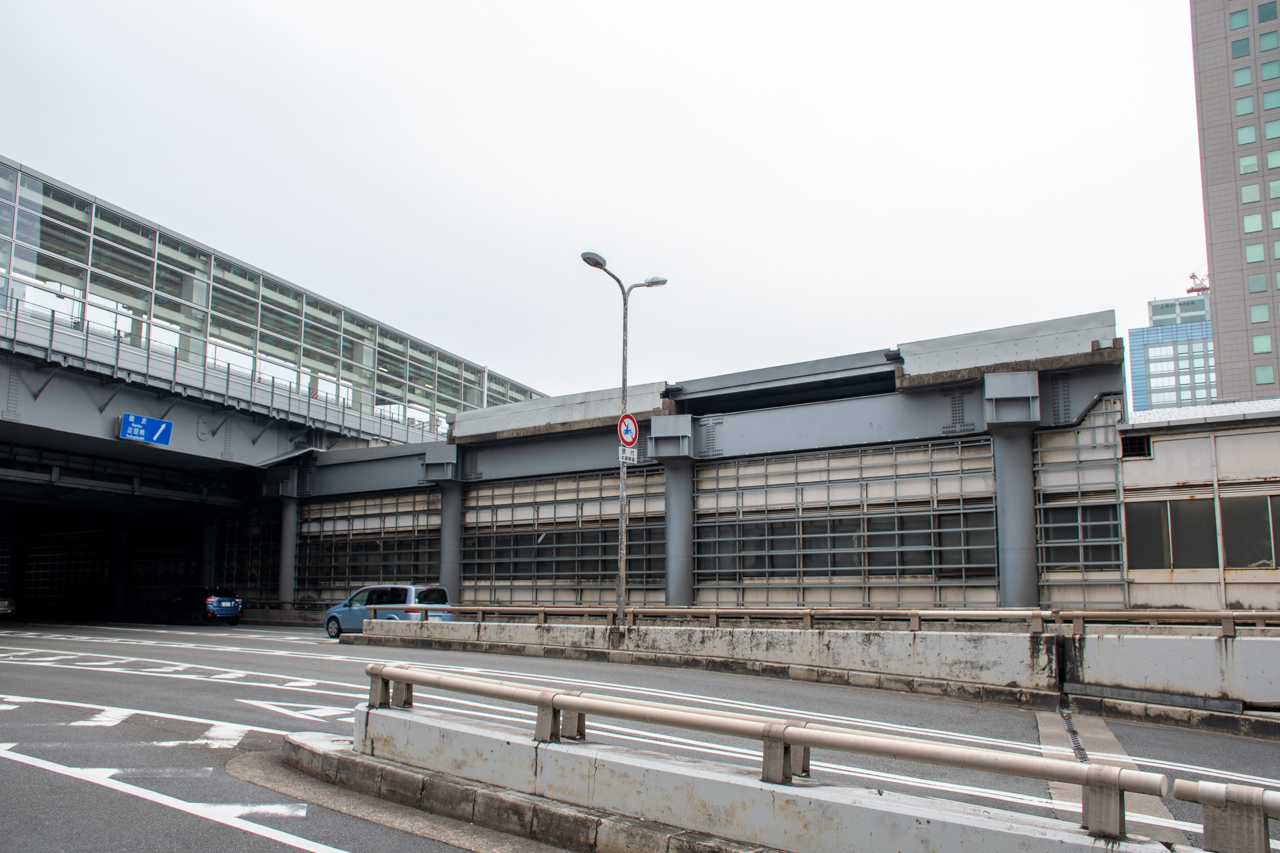 道路の奥にあるのは大阪メトロ御堂筋線の新大阪駅。左側で交差しているのは新幹線の新大阪駅です。御堂筋線の駅の上にある構造体は、阪急新大阪連絡線の建設にそなえて用意された橋脚です