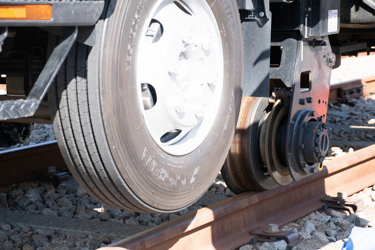 架線作業車の床下をアップ。鉄車輪がレールの上に乗っており、前タイヤは地面から離れているのがわかる。